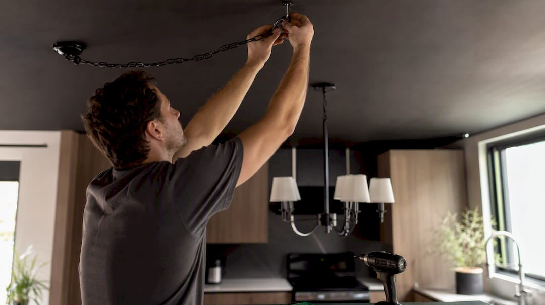 Hands installing ceiling hook for swaging chandelier