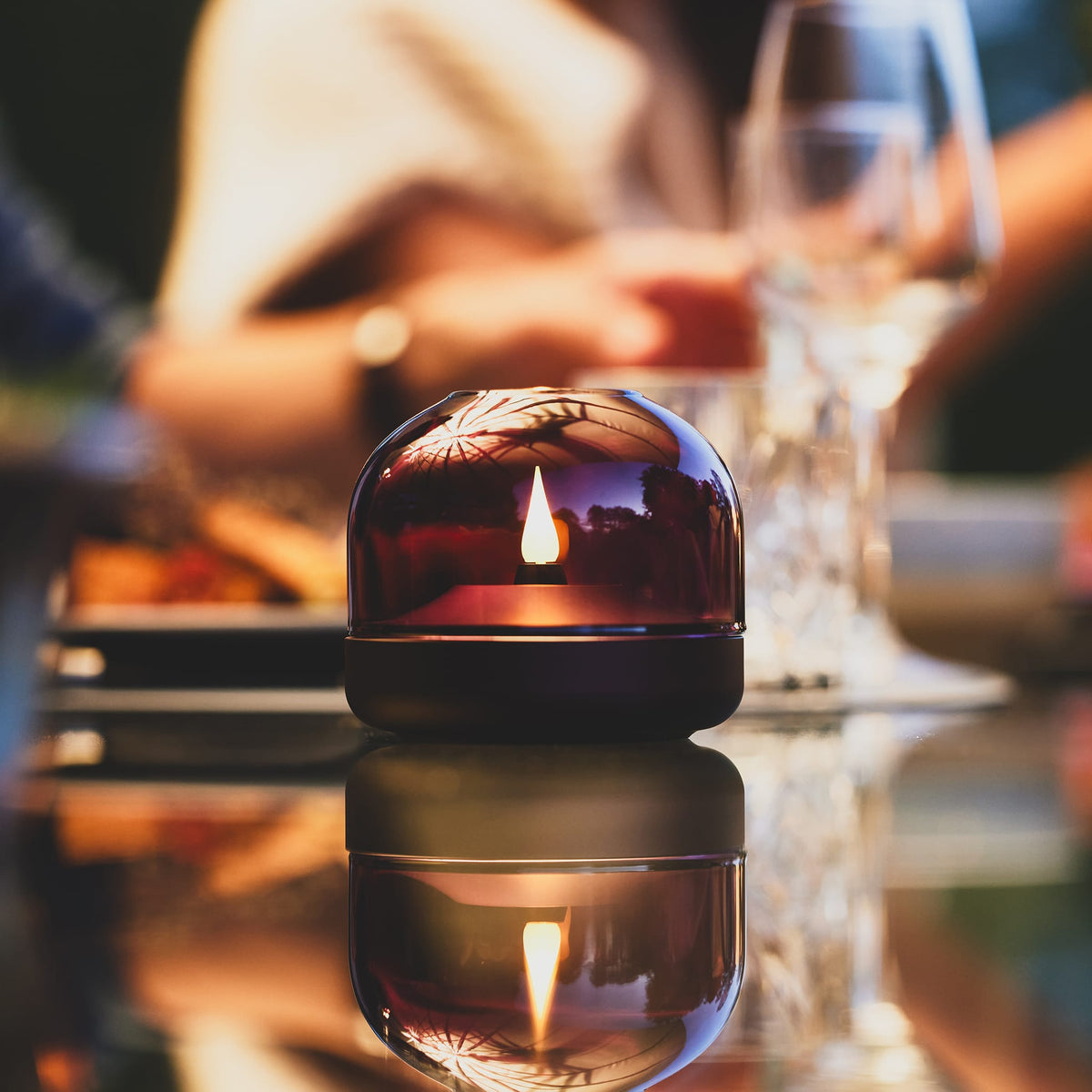 Glow 08 candle holder with LED flame, burgundy dome on a reflective glass table.