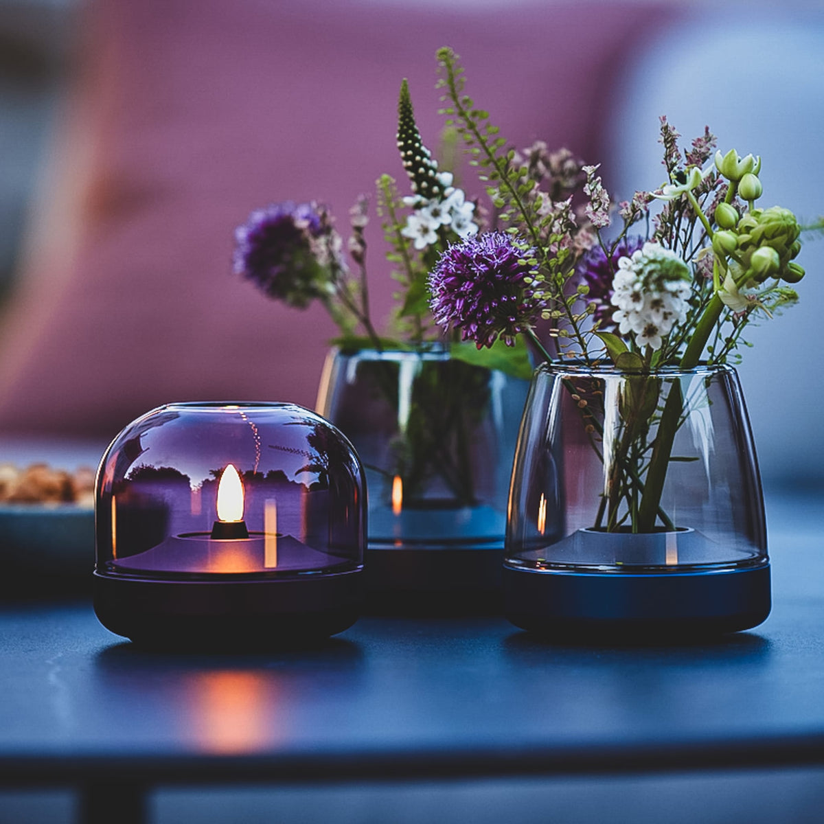 Glow 08 candle holder with a purple glass dome housing an LED candle, shown beside fresh flowers.